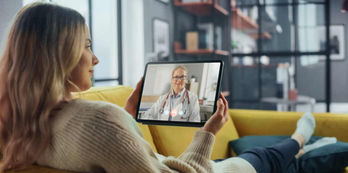 Woman on couch with tablet meeting with a doctor online.